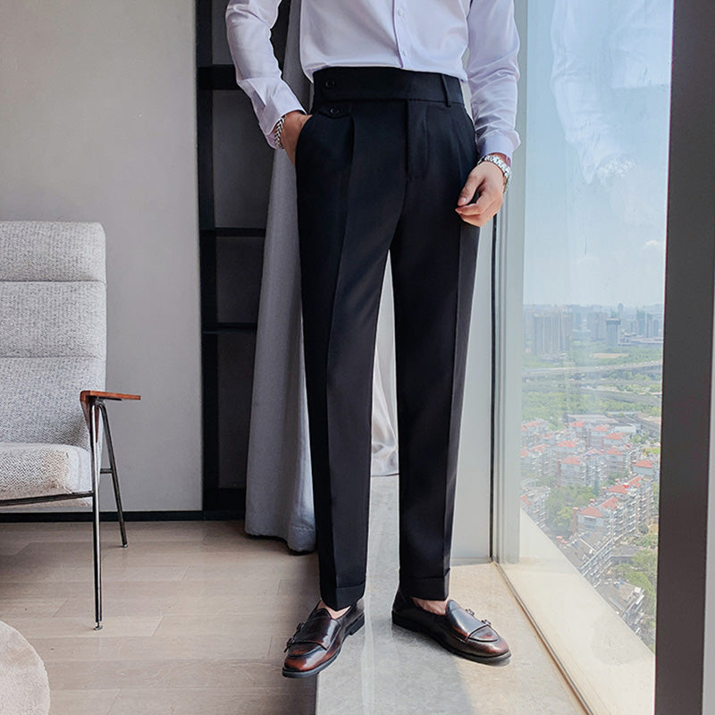 A man models Elysian black high-waisted slim-fit trousers made from premium fabric, paired with a white dress shirt. He stands by a large window overlooking a city skyline, showcasing the tailored finish and comfortable fit of the pants.