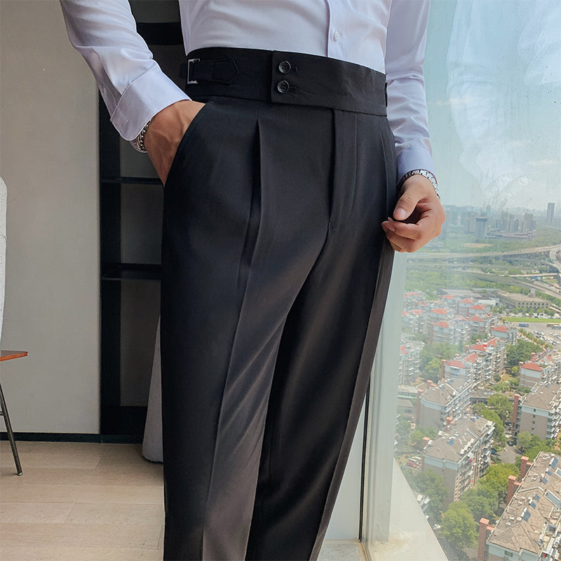 A man models Elysian black high-waisted slim-fit trousers, showcasing the tailored waist and functional pockets. He wears a white shirt and stands by a window with a city backdrop, emphasizing the smart casual appeal.