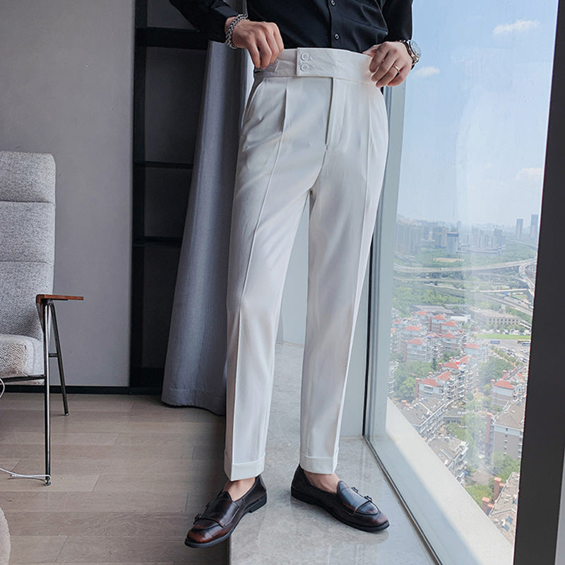 A man models Elysian white high-waisted slim-fit trousers made from premium fabric, paired with a black dress shirt. He stands by a large window overlooking a city skyline, highlighting the versatile and tailored design.