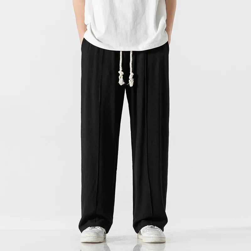 Elysium Drift black linen sweatpants with a relaxed fit, shown from the front with a visible drawstring, paired with a white t-shirt.