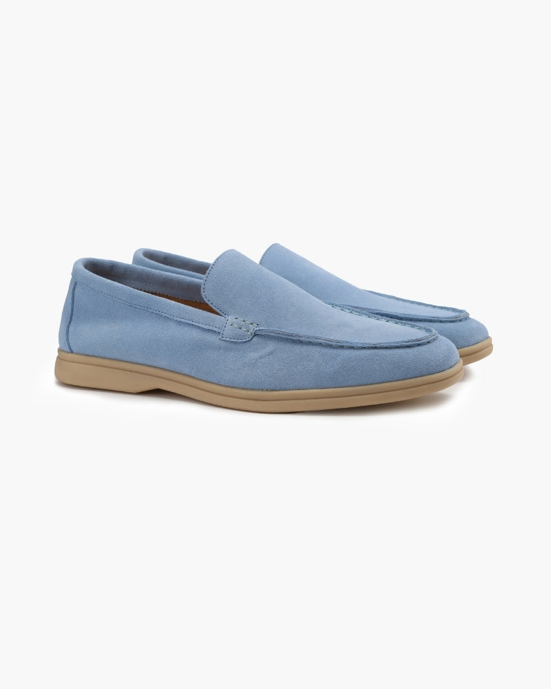 A pair of light blue suede men's loafers with classic stitching, featuring a tan sole, presented in a side view against a clean white background.