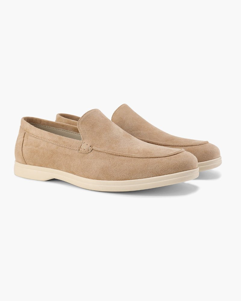 A pair of Heritage Luxe beige suede loafers with classic stitching, featuring a comfortable slip-on design and light-colored soles, presented from a side angle.