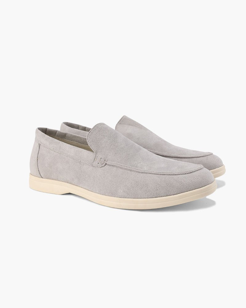 A pair of Heritage Luxe light gray suede loafers with classic stitching, featuring a comfortable slip-on design and light-colored soles, presented from a side angle.