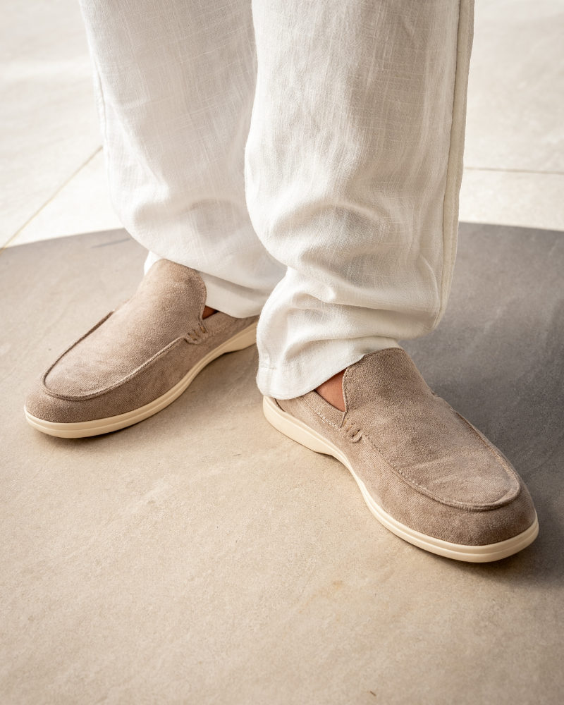 Men's Mocha Heritage Luxe Suede Loafers with Classic Stitching, worn with white pants while standing.