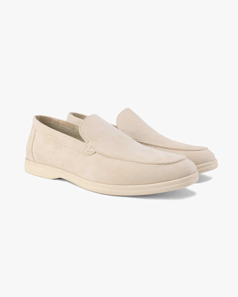 A pair of Heritage Luxe beige suede loafers displayed in a side view on a clean white background, showcasing their classic slip-on design.