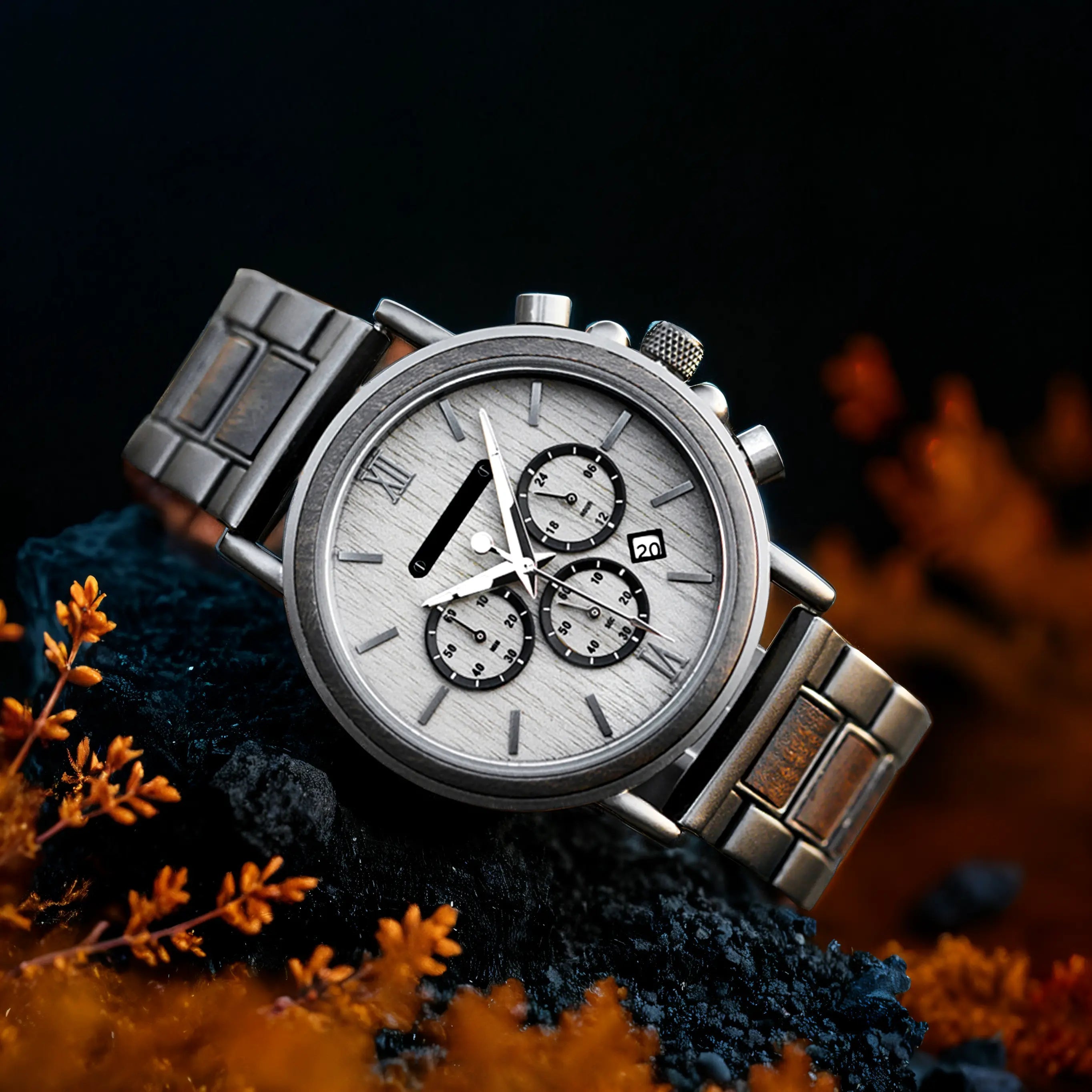 Close-up view of the Heritage Oak men's watch with a light dial and metal strap, resting on a dark textured surface with blurred orange foliage.