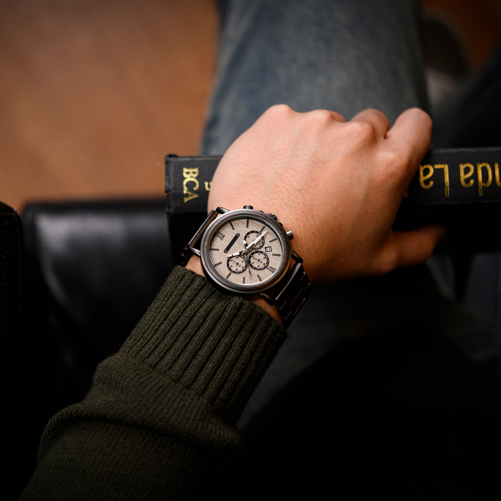 Heritage Oak men's watch with a light dial and metal strap worn on a man's wrist, holding a book.