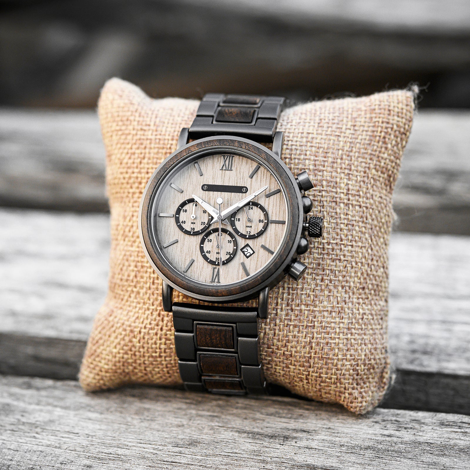 Heritage Oak men's watch with natural wood and dark metal band, displayed on a light brown burlap cushion on a rustic wooden surface.