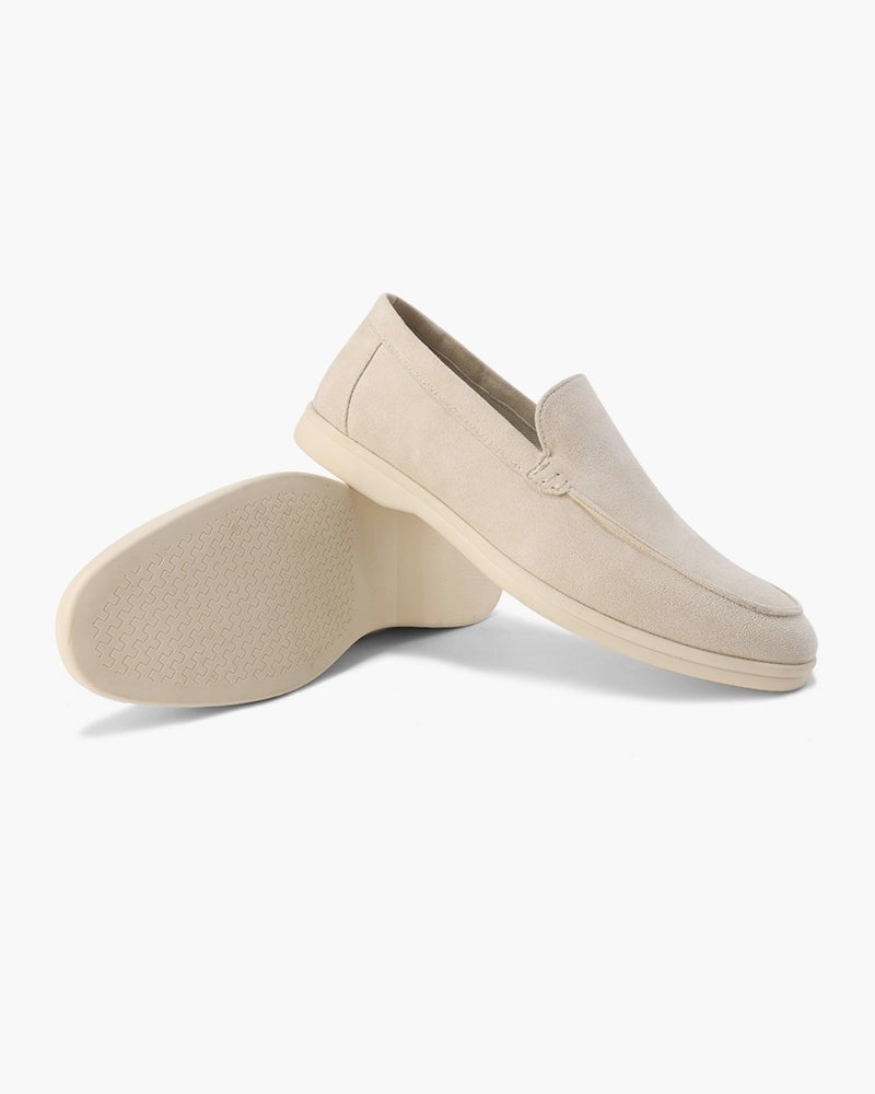 Pair of Heritage Luxe Beige suede loafers with classic stitching, one upright showing the top and side, the other on its side revealing the textured sole. White background.