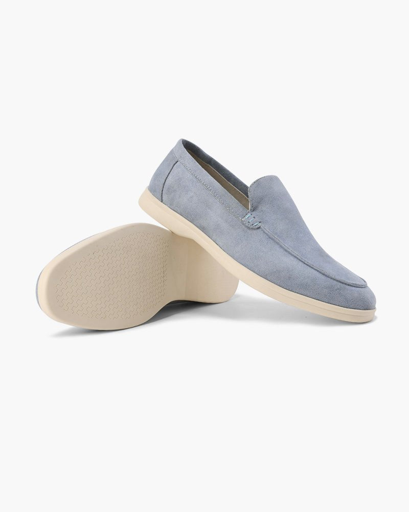 Pair of Heritage Luxe Fog Blue suede loafers with classic stitching, one upright showing the top and side, the other on its side revealing the textured sole. White background.