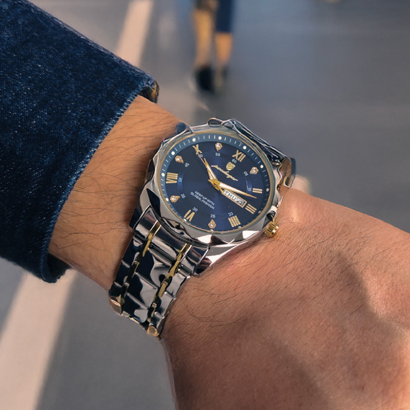 Maverick Luxe men's watch in stainless steel and gold, featuring a blue dial with date display and luminous hands, worn on a man's wrist with a denim jacket, walking on a street.