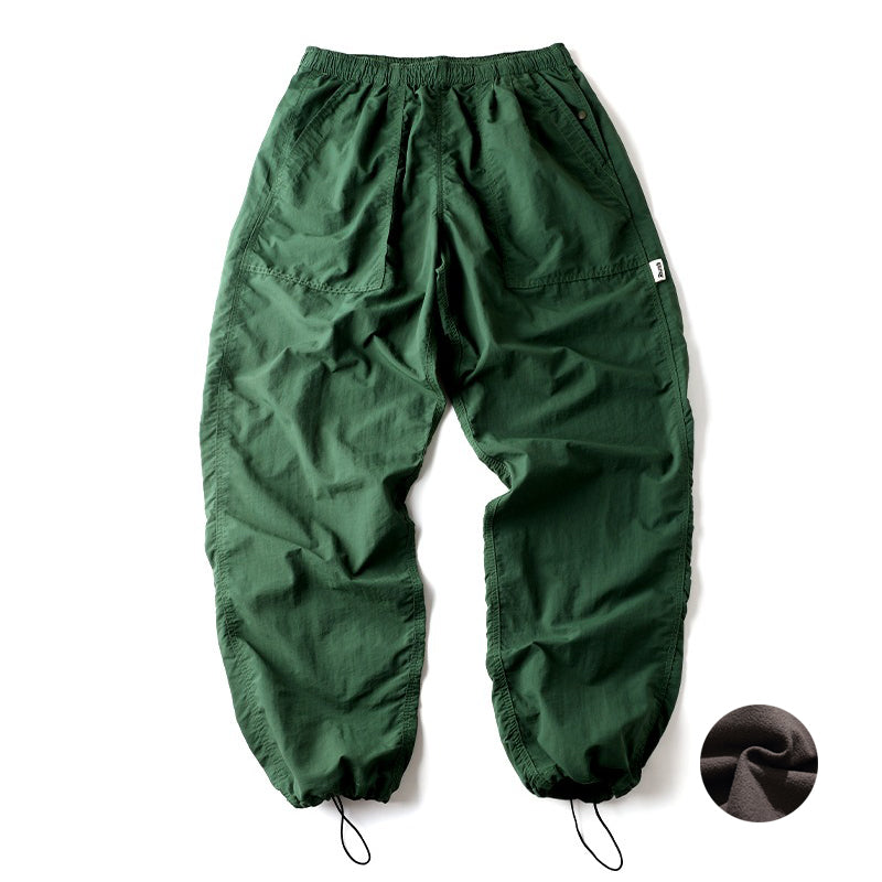 Green Sakura Breeze waterproof breathable casual pants with a relaxed fit, laid flat showing the front view. A small circular swatch of soft fleece fabric is shown in the bottom right corner, indicating a fleece-lined variant.