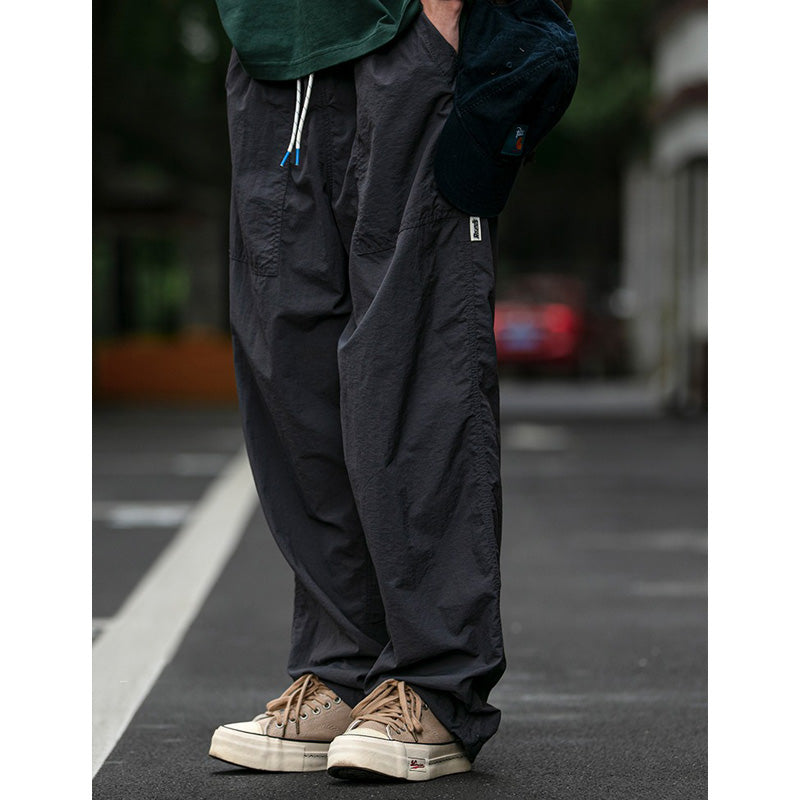 Side view of a man modeling Sakura Breeze waterproof, breathable, relaxed fit casual pants in deep grey, paired with a green t-shirt and holding a cap.