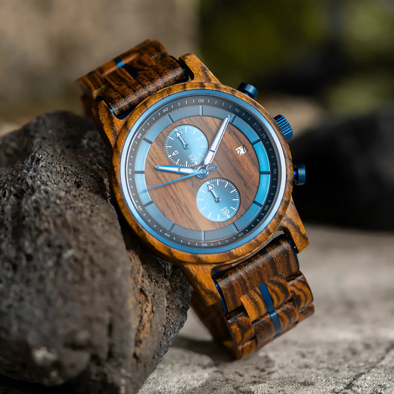 Serpentis men's watch in steel with blue dial, close-up view of the wooden watch with blue accents resting on a dark rock.