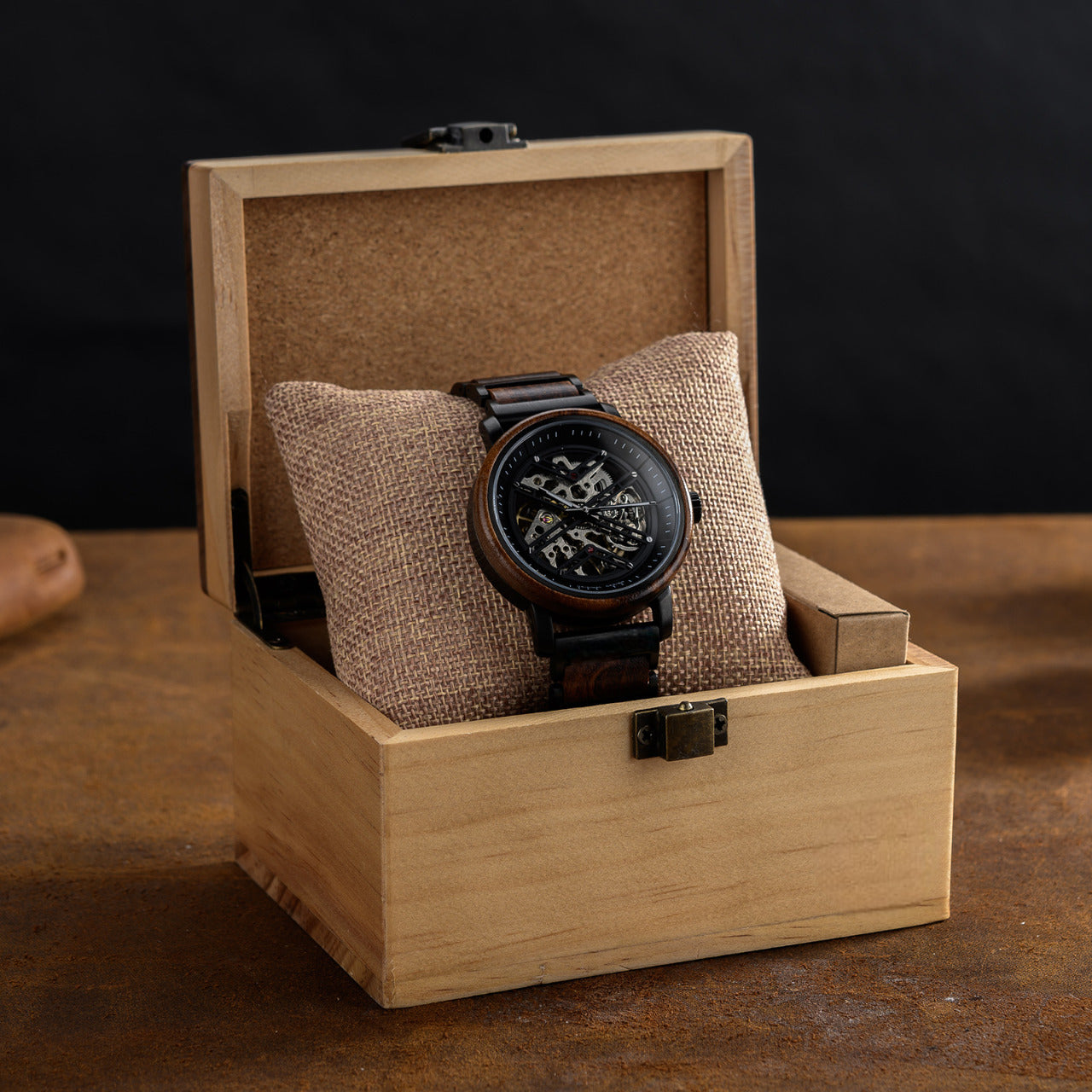 Terra Brown men's wooden watch natural finish displayed open light brown wooden gift box, resting on burlap cushion, showcasing its skeleton dial.