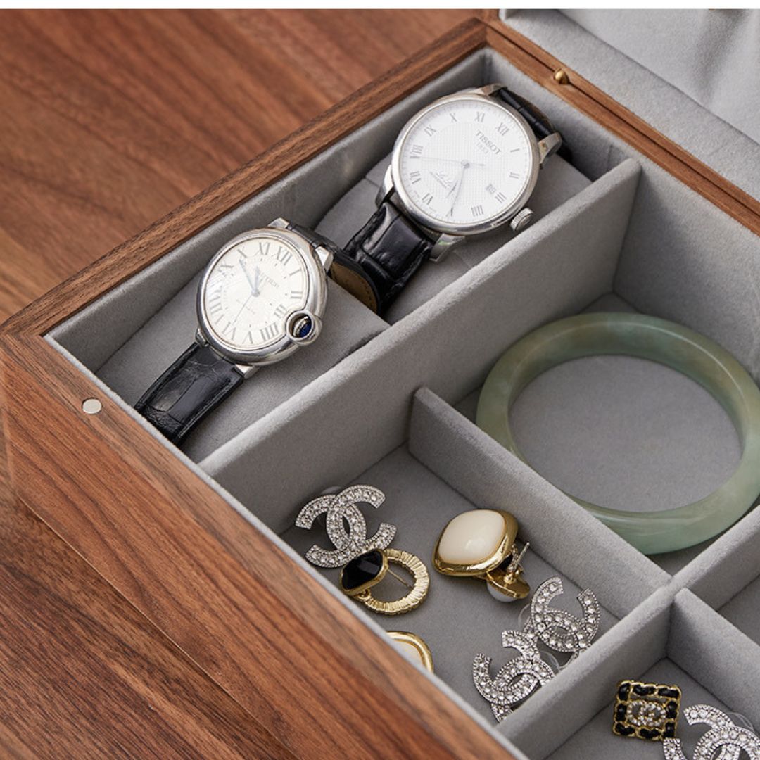 Close-up view of the open Timber Haven solid walnut wood jewelry box, showcasing two watches, a jade bangle, and various rings and earrings neatly organized in the grey velvet compartments.