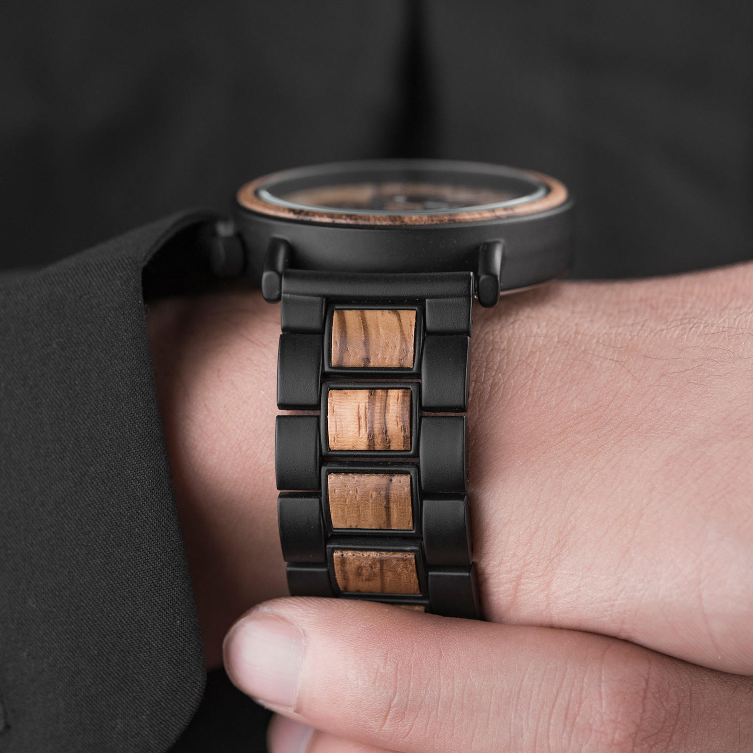 A man's wrist wearing the Timberlight men's wooden watch with a natural finish, showcasing the side profile of the watch and its distinctive wooden and black metal links against a dark shirt.