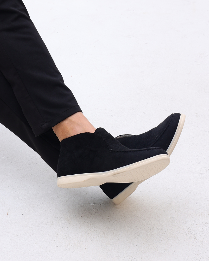 Black suede loafers with classic detailing worn by a person in black pants, captured from a side view.