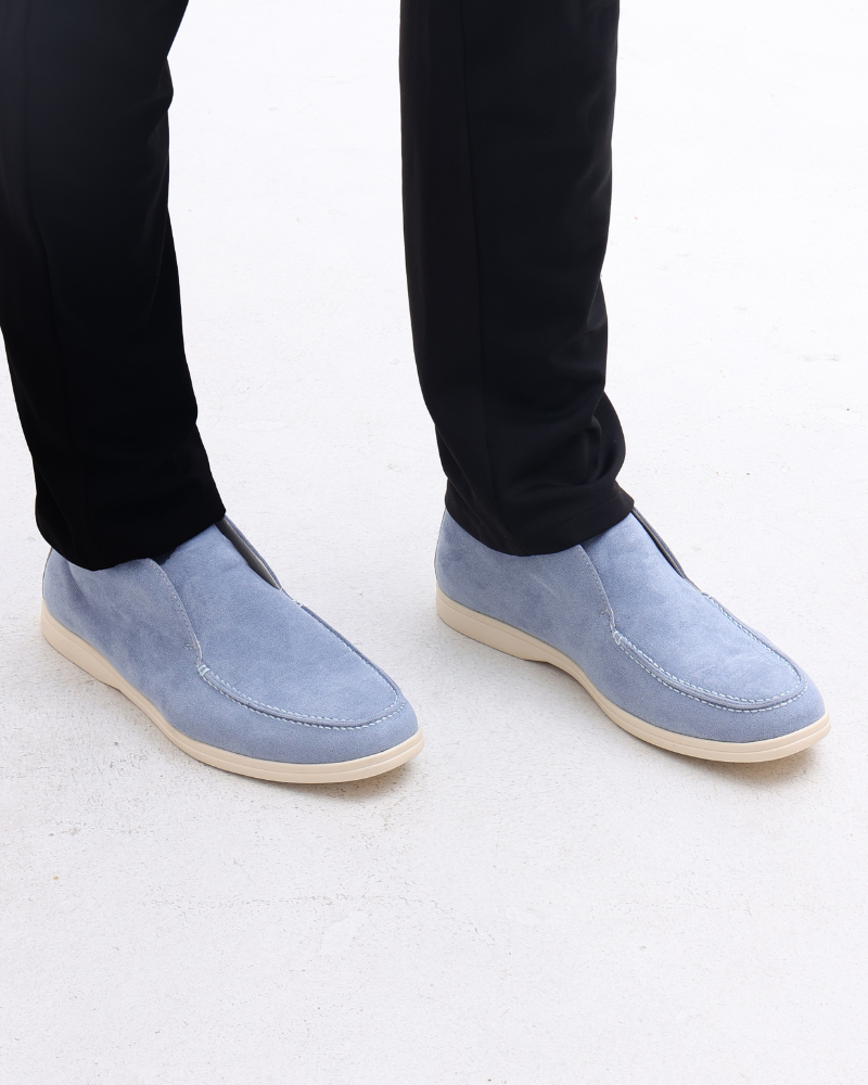 Fog blue suede loafers with classic detailing worn by a person in black pants, shown from a standing view.