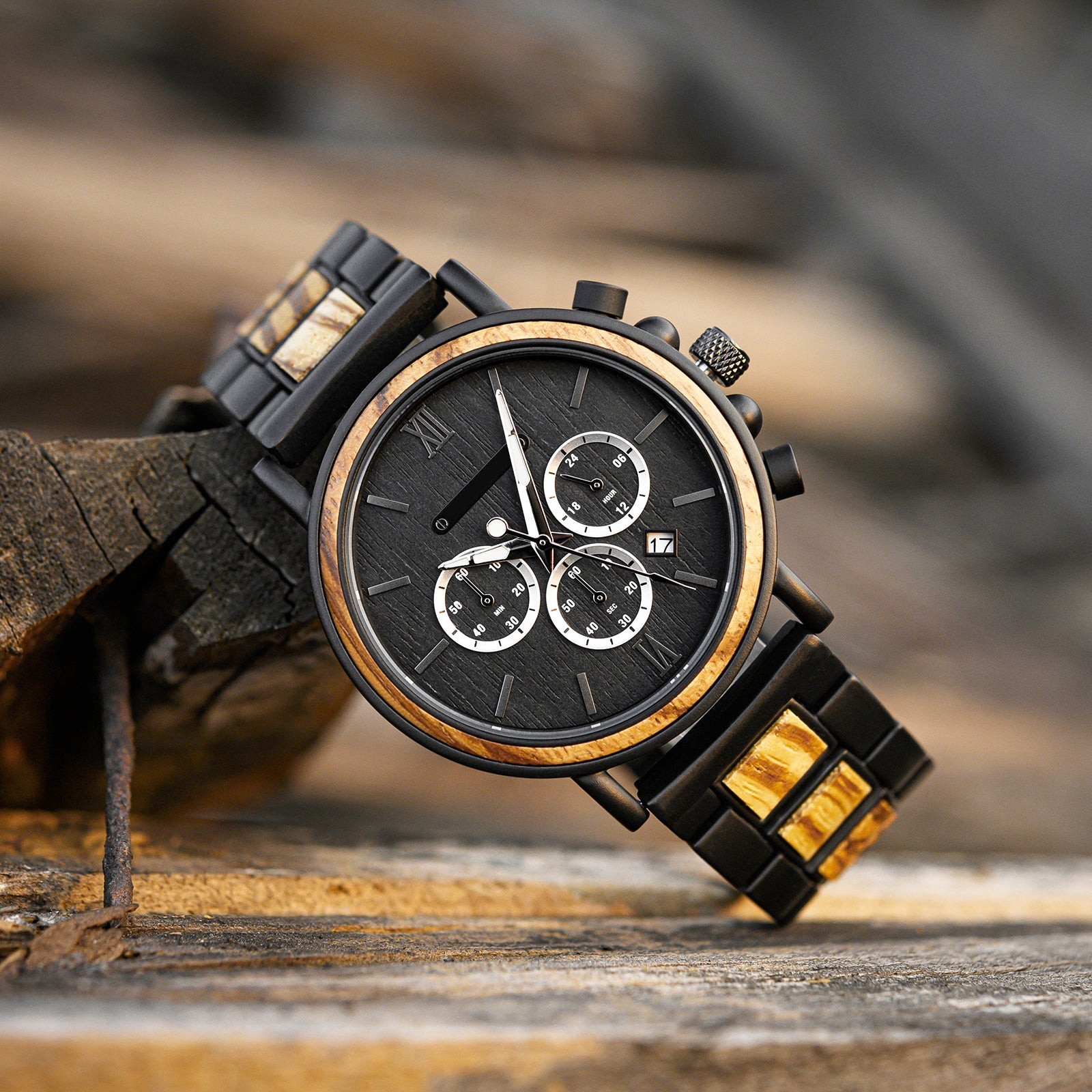 Close-up of the Timberline men's watch featuring a black dial, chronograph subdials, and a black band with whiskey oak wood accents, resting on a rustic wooden surface.
