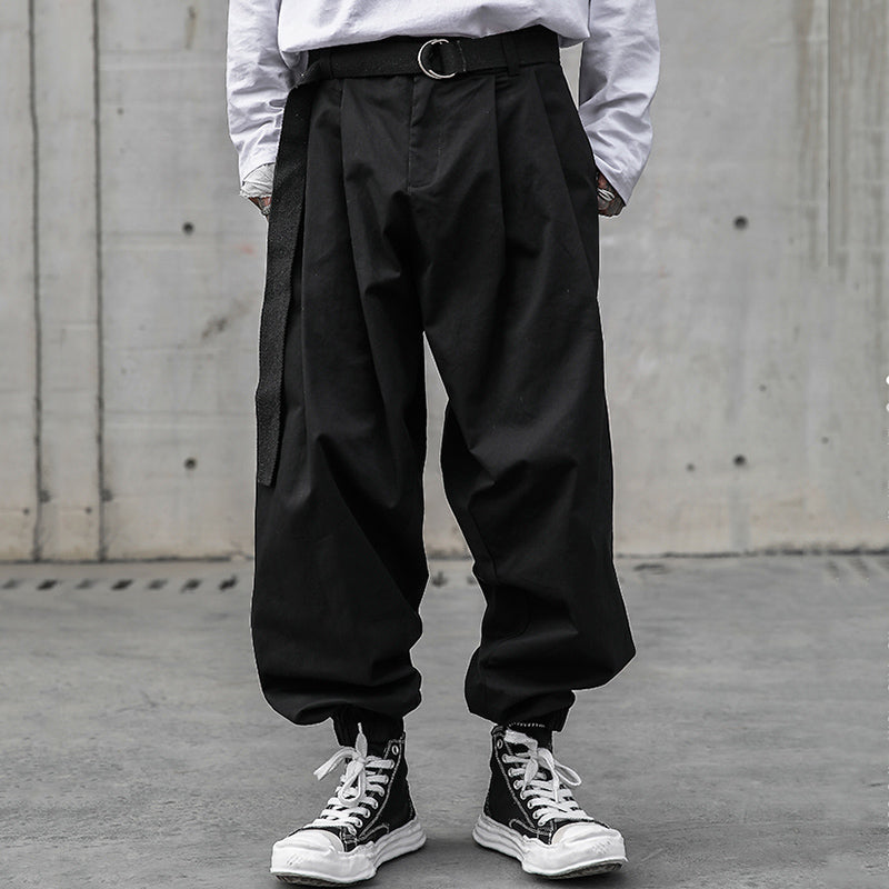 Urban Essence men's black baggy pleated pants with a retro design, elastic cuffs, and a black belt, shown on a male model from the front.