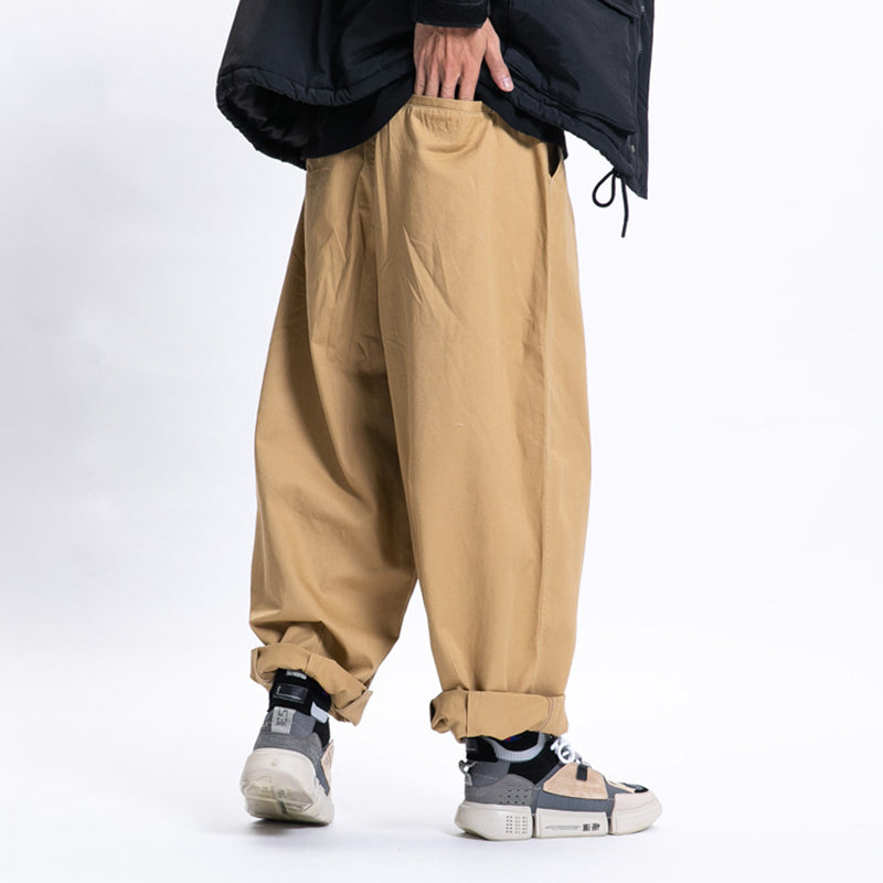 Male model wearing khaki Urban Luxe wide-leg casual pants made from soft fabric with a relaxed fit, cuffed at the ankles, with hand in pocket and paired with sneakers.
