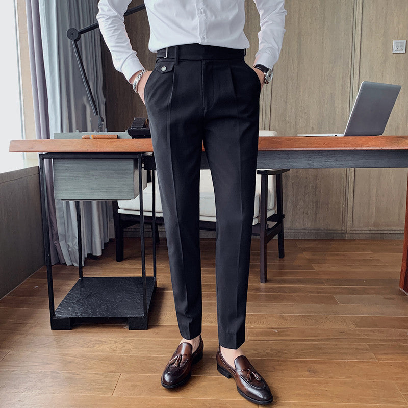A man models Vintage Charm men's retro black suit pants with a tailored fit and lightweight fabric, paired with a white shirt and brown loafers in an office setting. The pants feature a unique side buckle detail.