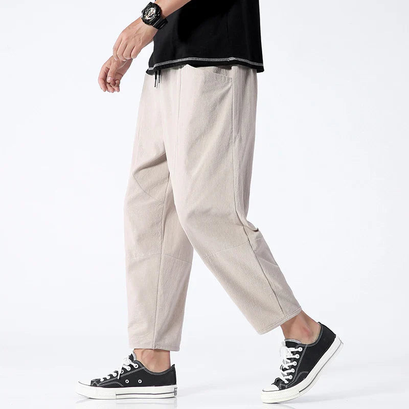 Male model showcasing Zenith Cropped Trousers in light khaki, made from a cotton-linen blend. The tailored finish pants are styled with a black t-shirt and black sneakers, highlighting their smart-casual appeal and lightweight, breathable fabric for men's summer fashion.