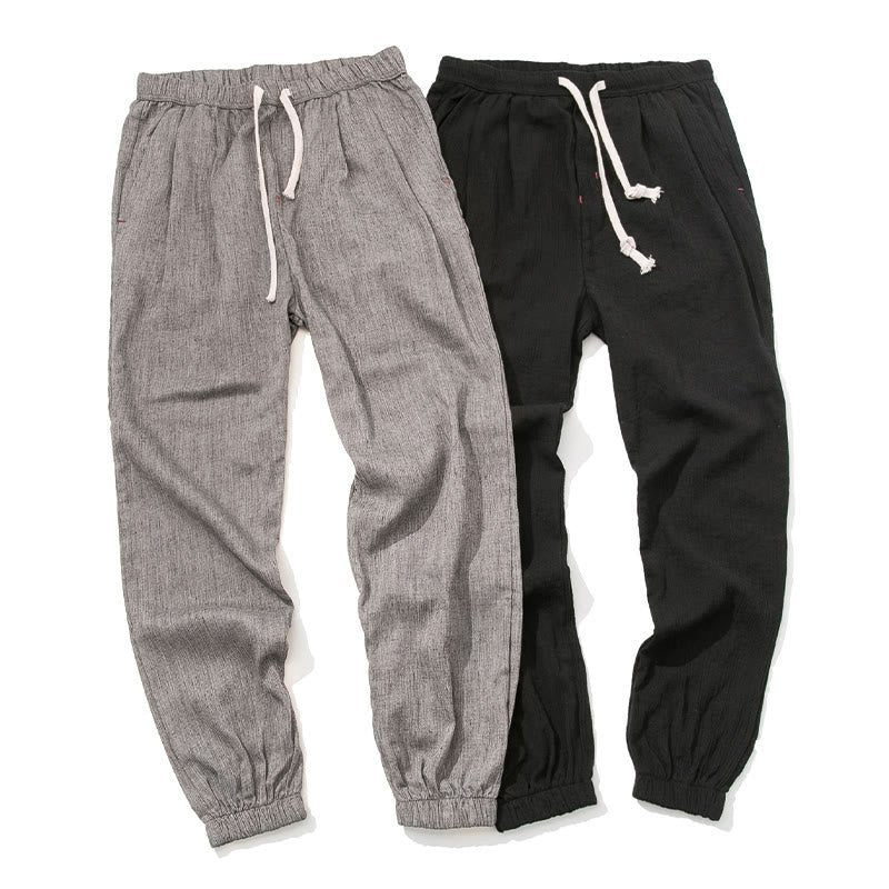 Flat lay of two pairs of Zenith Stones linen drawstring pants. One pair is Gray, and the other is Black, both featuring white drawstrings and elastic cuffs. The pants are laid out to show their texture and relaxed style.