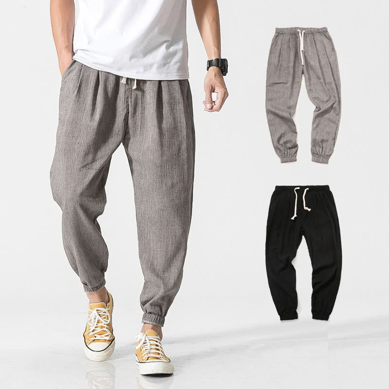 A man wearing Zenith Stones gray linen pants with a drawstring waist and side pockets, paired with a white t-shirt and yellow sneakers. To the right, two flat lay images show the gray and black versions of the linen pants.