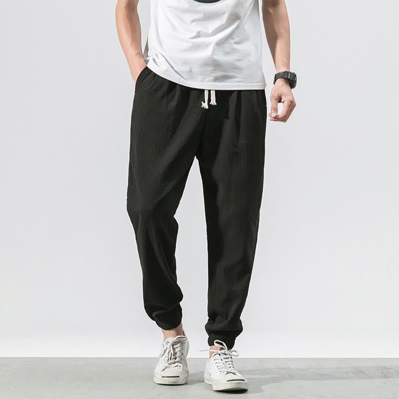 A man wearing Zenith Stones black linen pants with a drawstring waist and side pockets, paired with a white t-shirt and white sneakers.