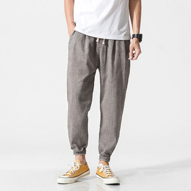 Full shot of a man wearing Zenith Stones gray linen men's pants with a drawstring waist and elastic cuffs, paired with a white t-shirt and yellow sneakers.