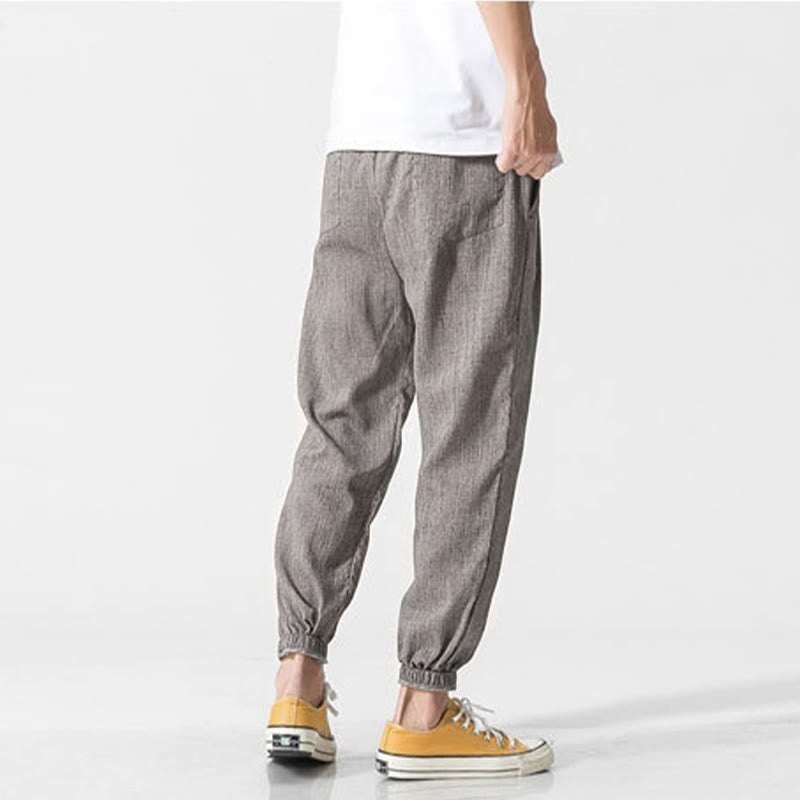 Zenith Stones men's gray linen pants with drawstring and side pockets, worn by a man in a white t-shirt and yellow sneakers, shown from a back-side view. Highlights the relaxed fit and casual design.