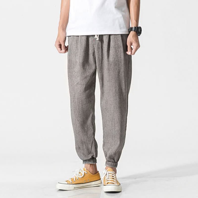 Zenith Stones men's gray linen pants with drawstring and side pockets, worn by a man in a white t-shirt and yellow sneakers, standing straight, front view. Showcases relaxed style and comfortable fit.