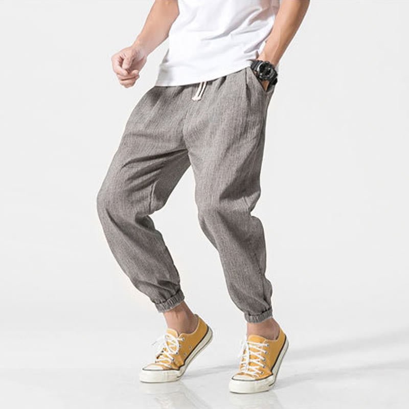 Zenith Stones men's gray linen pants with drawstring and side pockets, worn by a man in a white t-shirt and yellow sneakers, posing with hand in pocket. Ideal for casual wear, summer fashion, and comfortable fit.